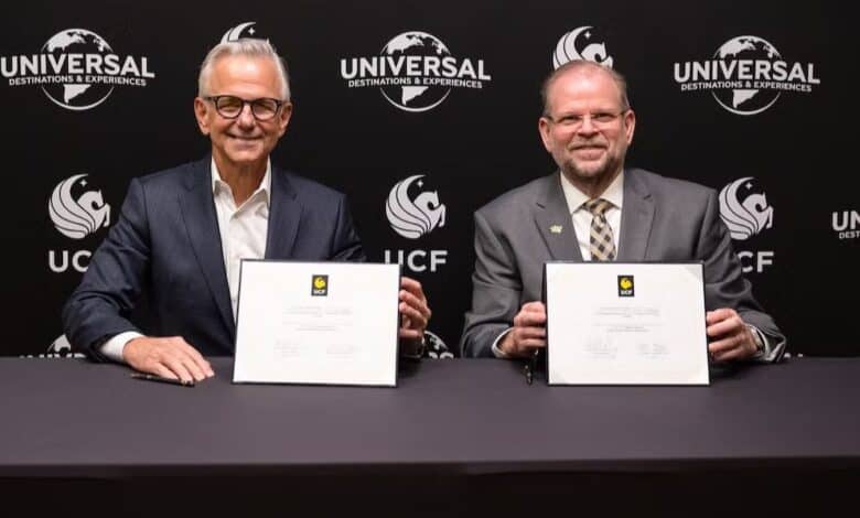 Universal and UCF executives signing documents at a table, with Universal and UCF logos displayed prominently behind them.