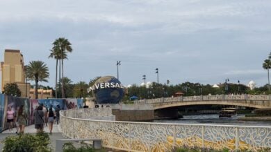 Guests stroll past vibrant murals and over a scenic bridge with the iconic Universal globe shining at Universal Orlando Resort.