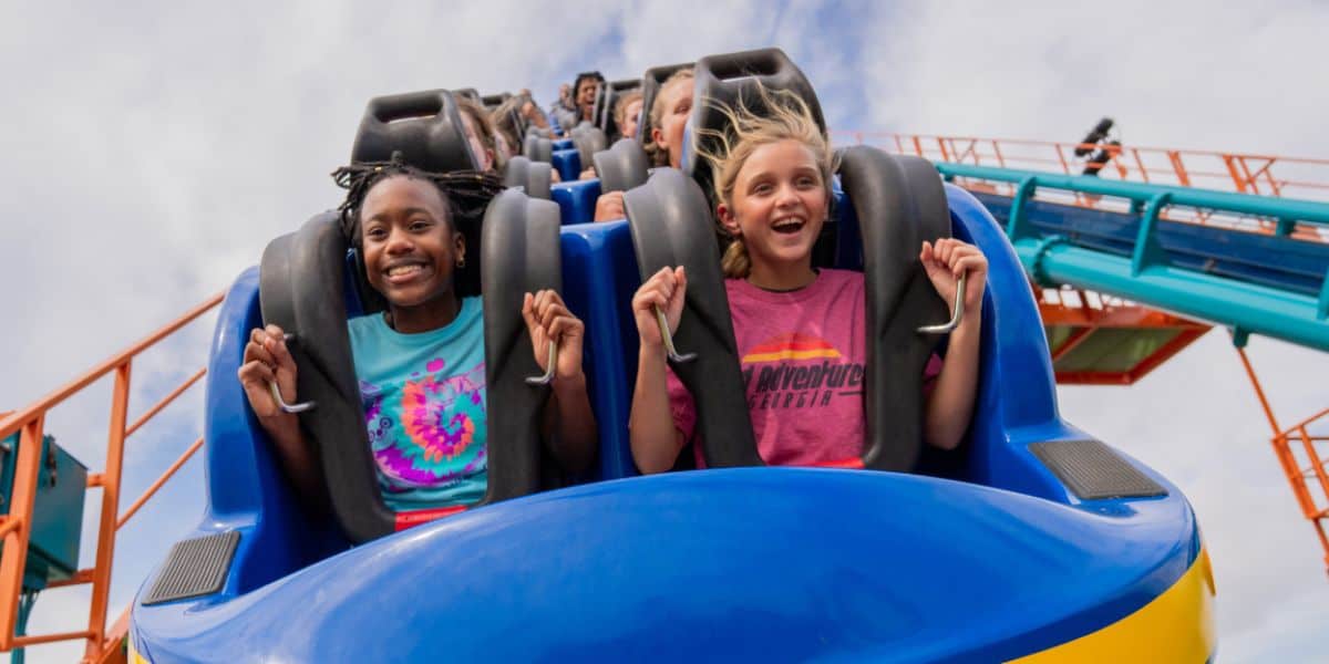 Guests enjoying a thrilling ride on the blue coaster at Six Flags Over Georgia beneath a partly cloudy sky.