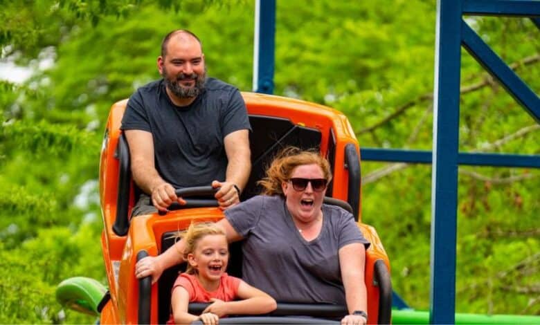 Guests laugh and smile as they race along Wildcat at Six Flags Over Georgia, surrounded by lush trees and blue sky.