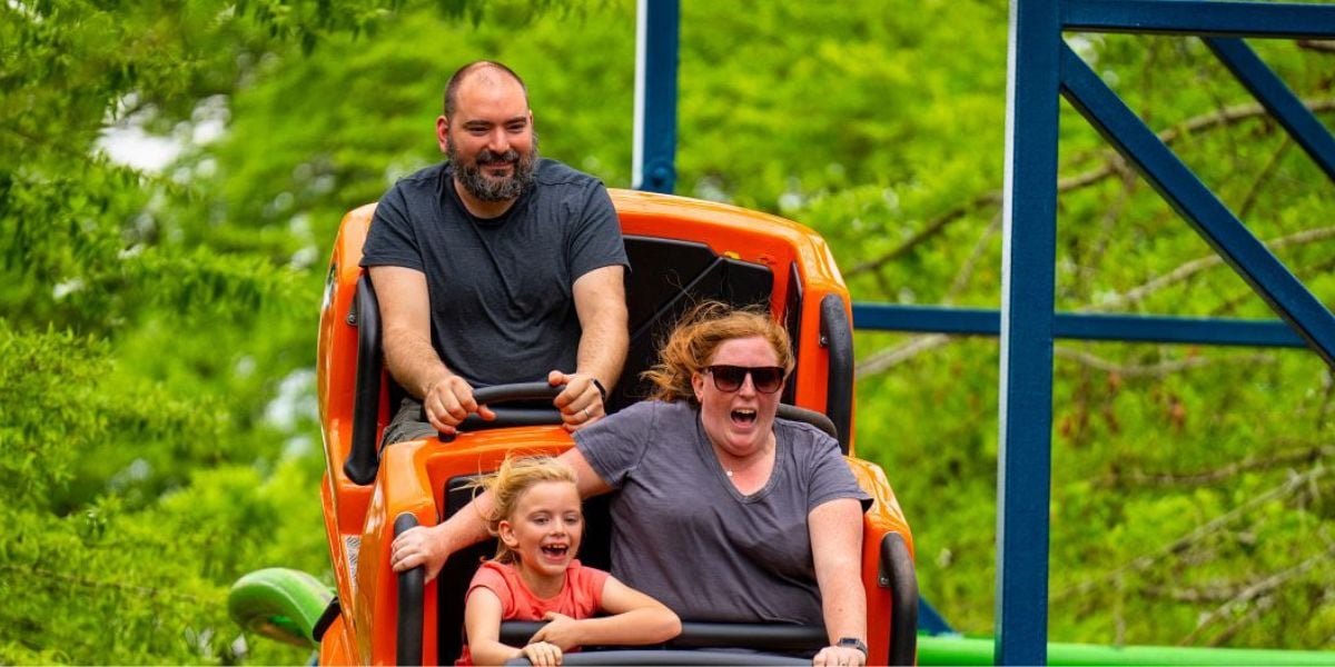 Guests laugh and smile as they race along Wildcat at Six Flags Over Georgia, surrounded by lush trees and blue sky.