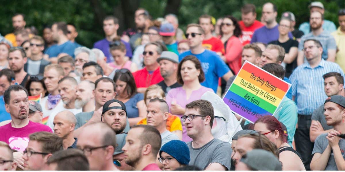 A crowd rallies as someone’s rainbow sign links LGBTQ rights, gun control, and Disney World’s connection to the Pulse tragedy.