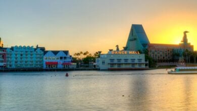 Sunset over Disney Springs with its vibrant waterfront, entertainment venues, and a boat cruising past lively themed buildings.