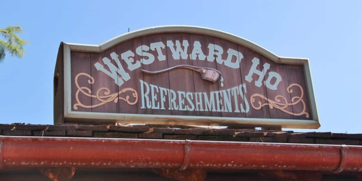 The "Westward Ho Refreshments" wooden sign stands out under a clear blue sky in Frontierland at Magic Kingdom.