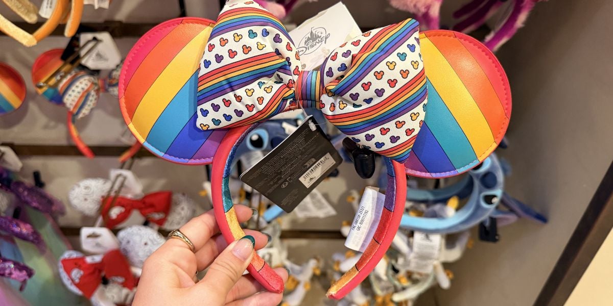 Rainbow-striped Mickey Mouse ears with a heart bow featured in a Disney store display, highlighting Pride Month festivities.