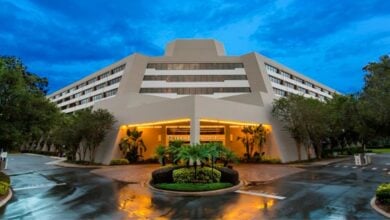 Contemporary Disney hotel with grand entrance, palm trees, and lush grounds—unlock magical rewards for your park adventure.