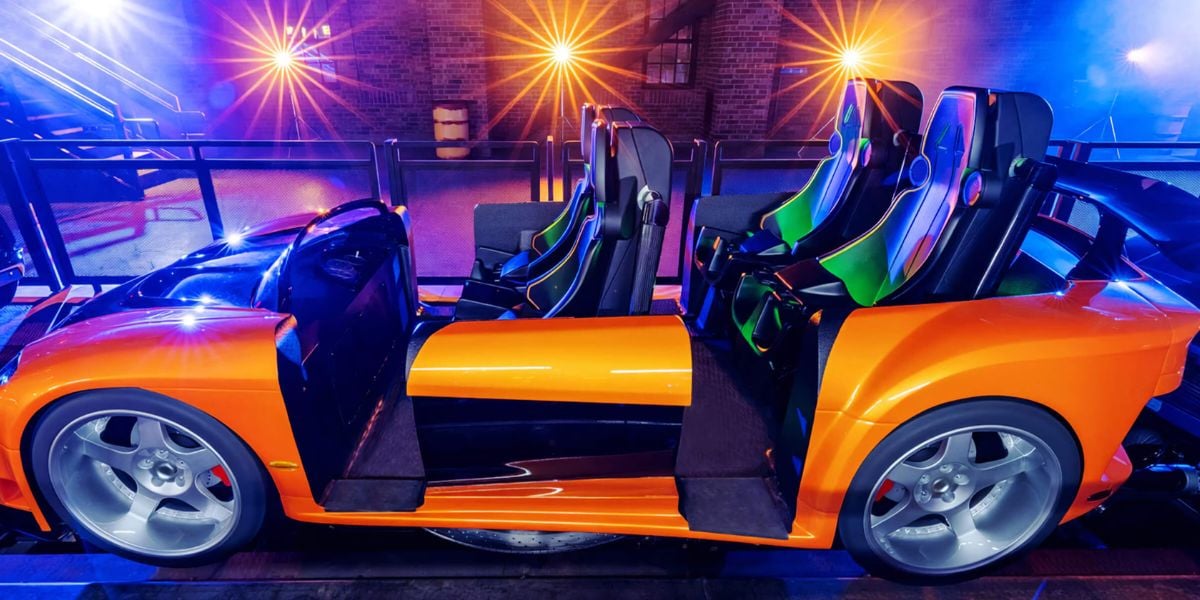 Exciting orange coaster car with two seats, glowing neon lights, and vibrant indoor fairground backdrop.
