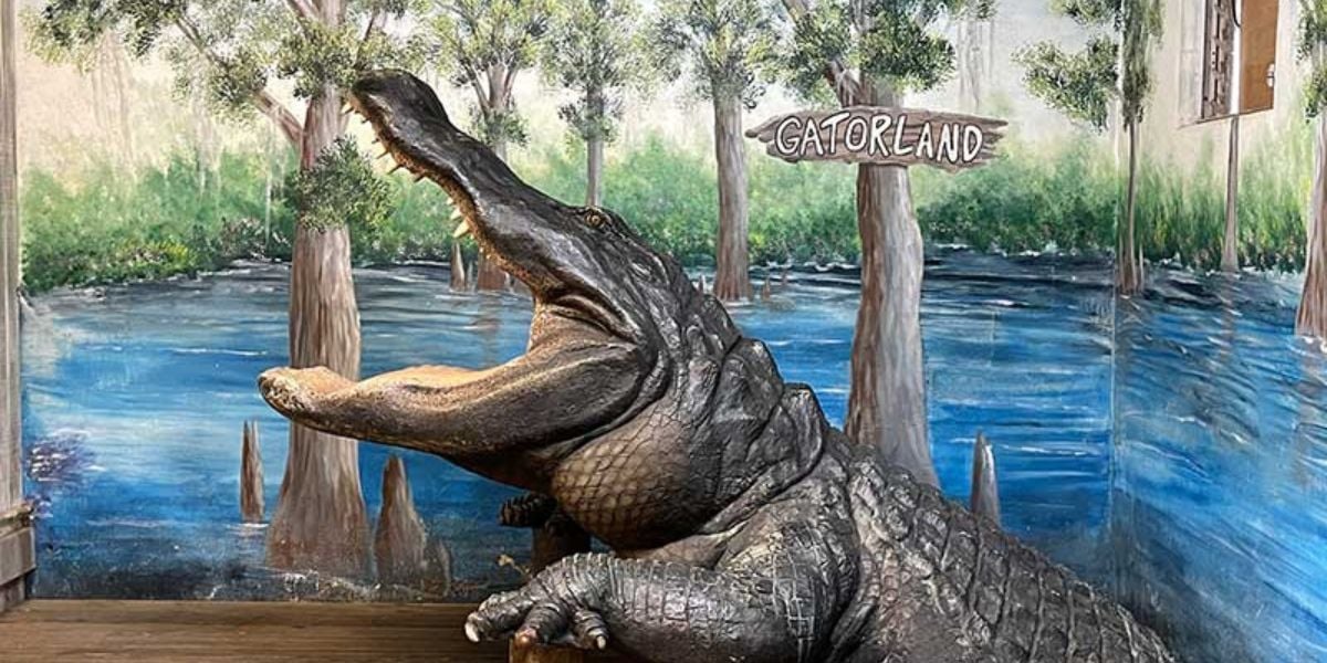Gatorland’s iconic open-jawed alligator statue welcomes guests in front of the vibrant Gatorland swamp mural.