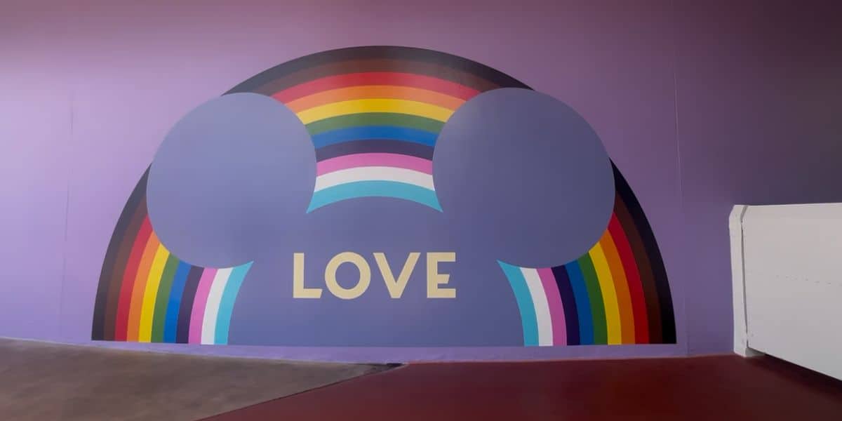 A vibrant mural featuring Mickey Mouse ears, a rainbow, and "LOVE" on a purple wall celebrates Pride Month at Disney Parks.