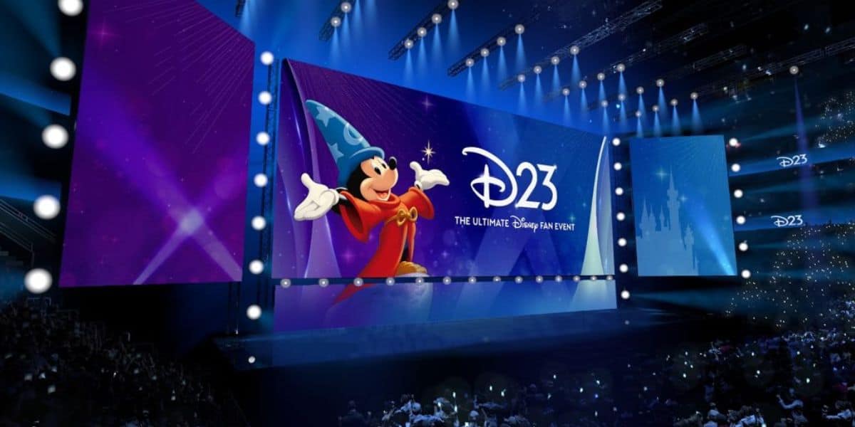 Sorcerer Mickey stands center stage as “D23: The Ultimate Disney Fan Event” lights up the massive screen, while an enthusiastic crowd of Disney fans eagerly awaits the next magical announcement at D23.
