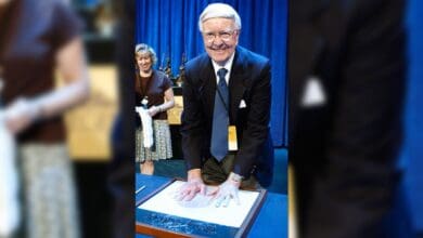 A well-dressed guest immortalizes his handprints in clay during a special ceremony, capturing the spirit of Disney’s timeless tributes. The scene unfolds with a supportive companion nearby and the signature blue draping found at many Disney Parks events, evoking magical memories of Mary Poppins for fans and visitors alike.
