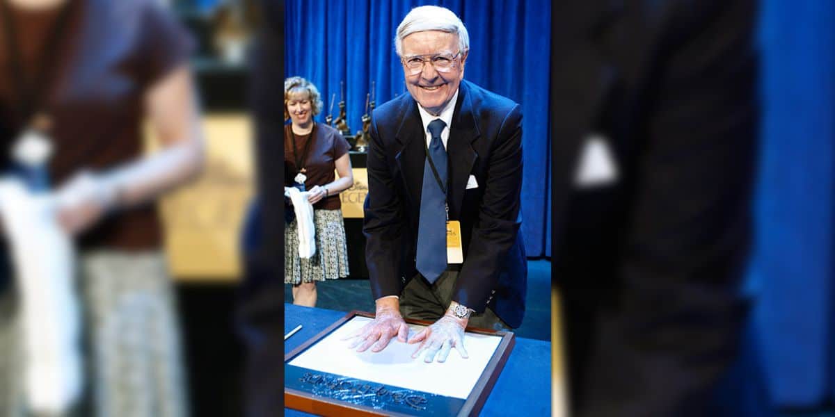 A well-dressed guest immortalizes his handprints in clay during a special ceremony, capturing the spirit of Disney’s timeless tributes. The scene unfolds with a supportive companion nearby and the signature blue draping found at many Disney Parks events, evoking magical memories of Mary Poppins for fans and visitors alike.