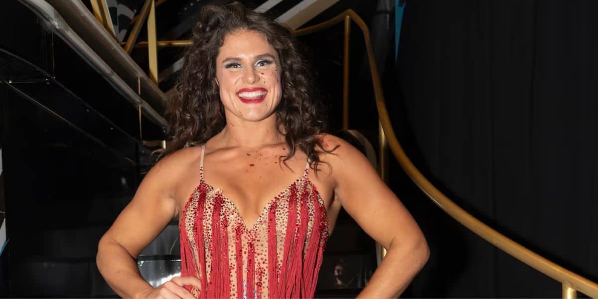 Glamorous performer in a shimmering red dress strikes a pose with one hand on her hip by the grand staircase at the venue.