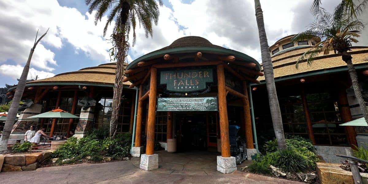 Thunder Falls Terrace entrance at Universal’s Islands of Adventure, framed by towering palm trees and a dramatic, cloudy sky overhead.