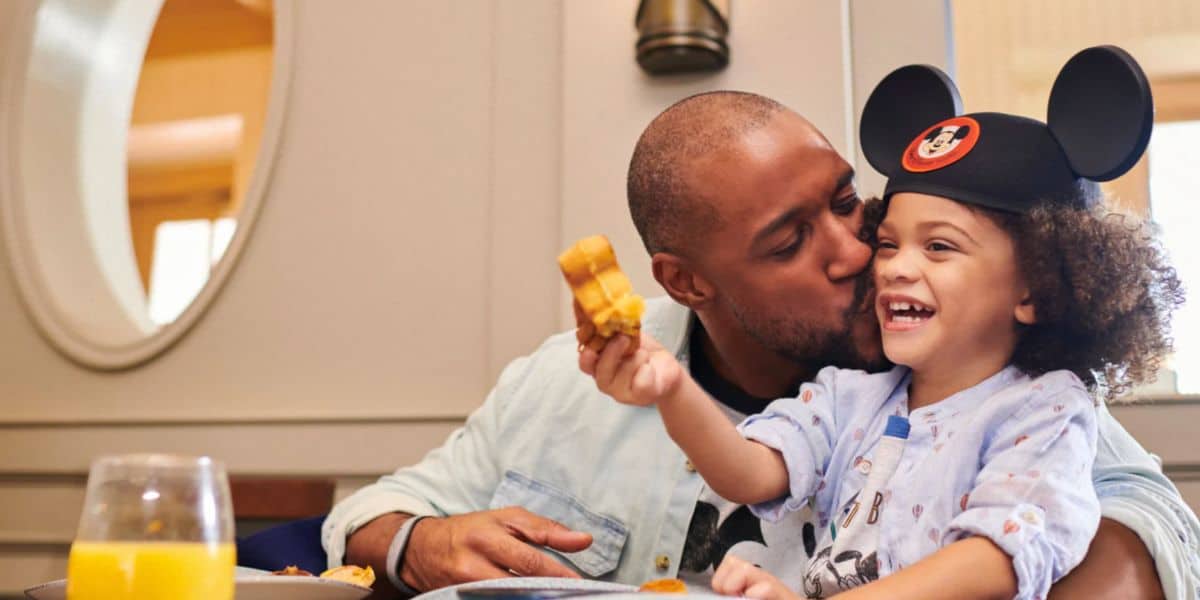 Mickey Mouse shares a magical breakfast moment with a beaming young fan at Disney World, as the child wearing iconic Mickey ears enjoys a fresh waffle and orange juice, highlighting the joy of family dining deals for theme park visitors.