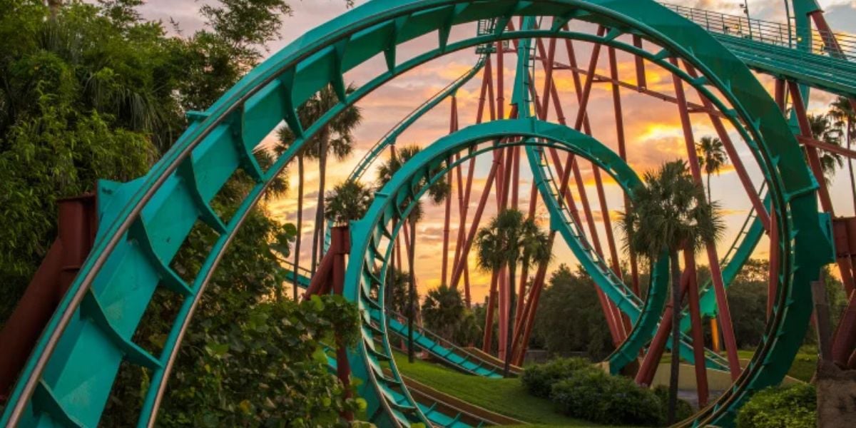 The thrilling Kumba roller coaster at Busch Gardens Tampa Bay twists through loops and spirals, its teal track shining against a vibrant sunset and swaying palm trees.
