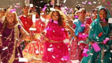 Dancers in vibrant traditional costumes perform energetically on a lively parade float as pink and white confetti showers the crowd, capturing the electric energy of an entertainment spectacular like a Cheetah Girls reunion at Universal Studios.