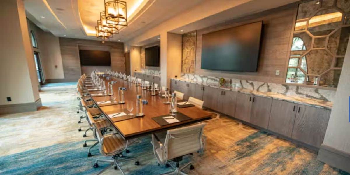 Conference room inspired by theme park creativity, featuring a long table, rows of chairs, large digital screens, and neatly arranged notepads—set up for an entertainment team to brainstorm new guest experiences after Disney World announces resort area activity closures.