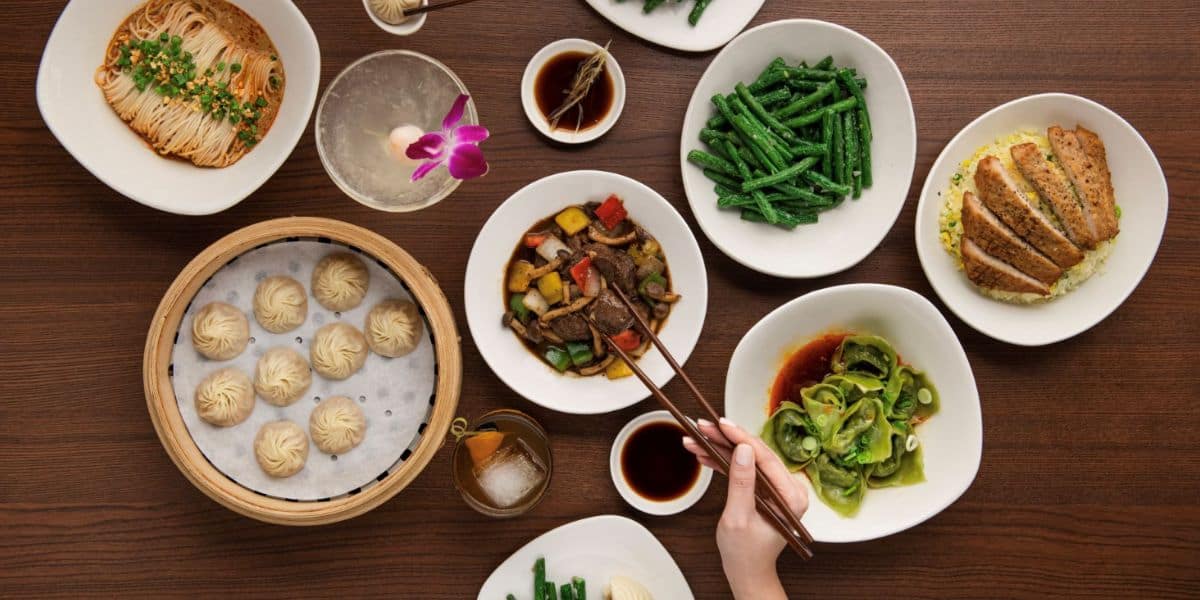 A colorful spread of Asian cuisine—dumplings, noodles, veggies, and drinks—served with chopsticks in Downtown Disney.