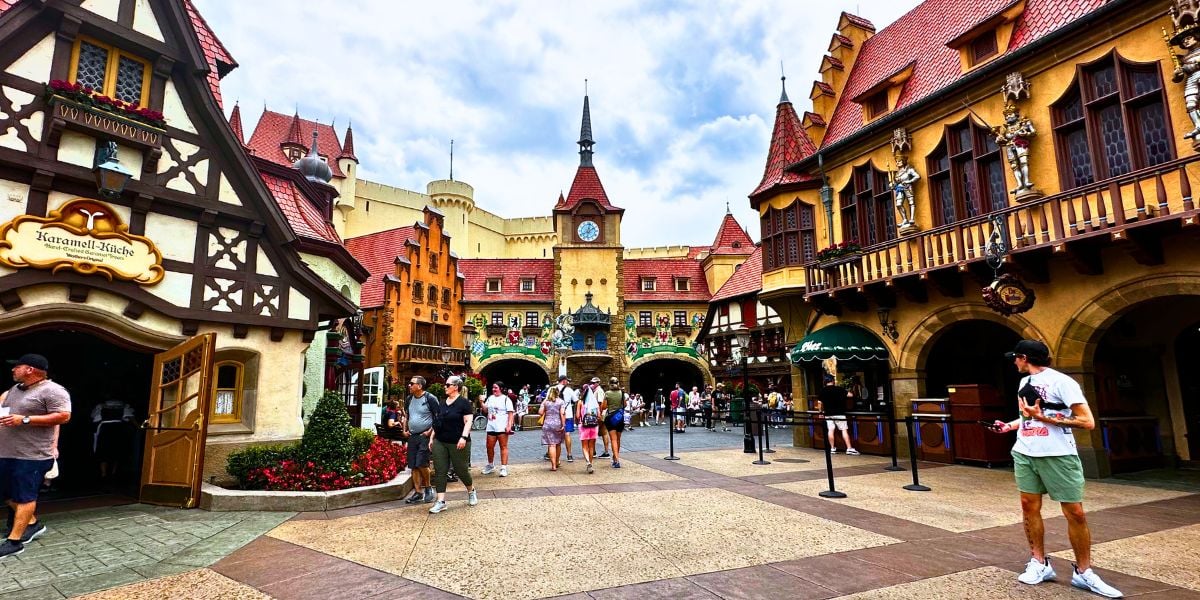 Guests stroll through the bustling Germany Pavilion at EPCOT, surrounded by vibrant, storybook buildings and a picturesque clock tower that capture the charm of a European village square.