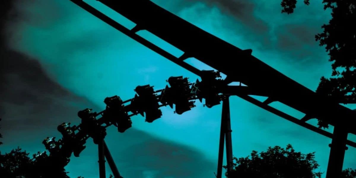 SeaWorld Orlando’s iconic roller coaster in silhouette, packed with excited riders soaring against a vibrant teal sky streaked with scattered clouds, capturing all the pulse-pounding excitement of a day at the park.