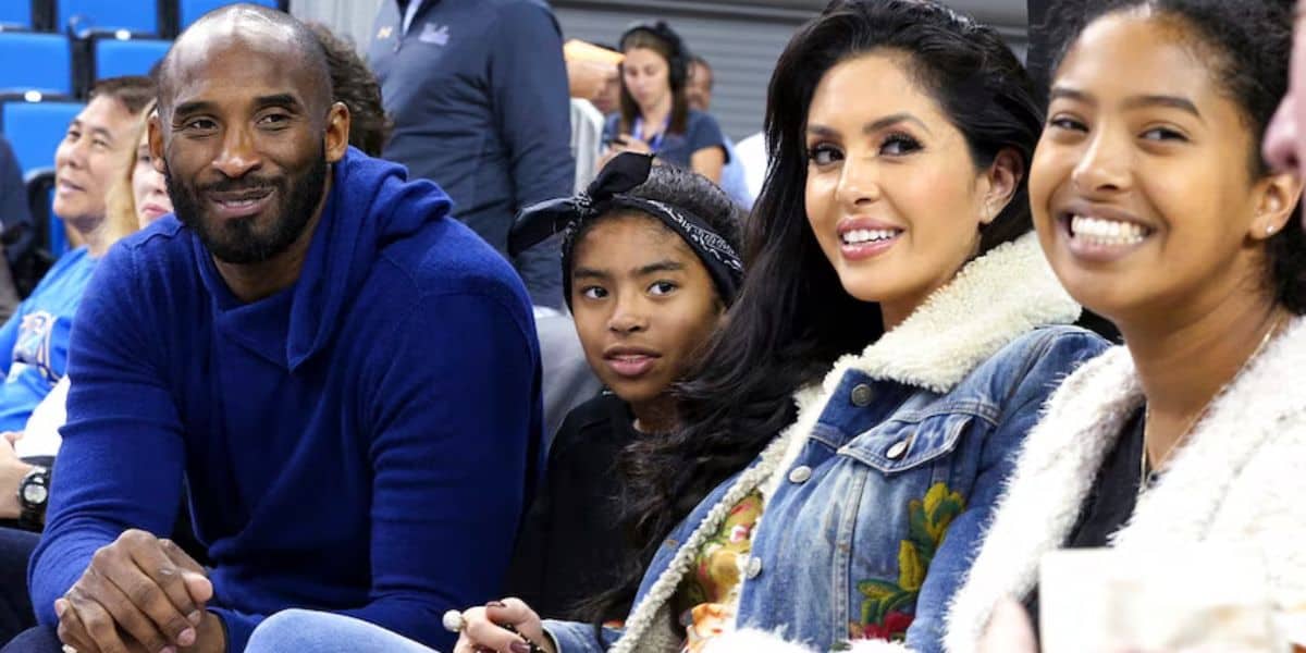 Vanessa Bryant and three companions share a joyful moment courtside at a basketball game, smiling for the camera in a scene filled with the emotional spirit of Disney’s moving Kobe Tribute event.