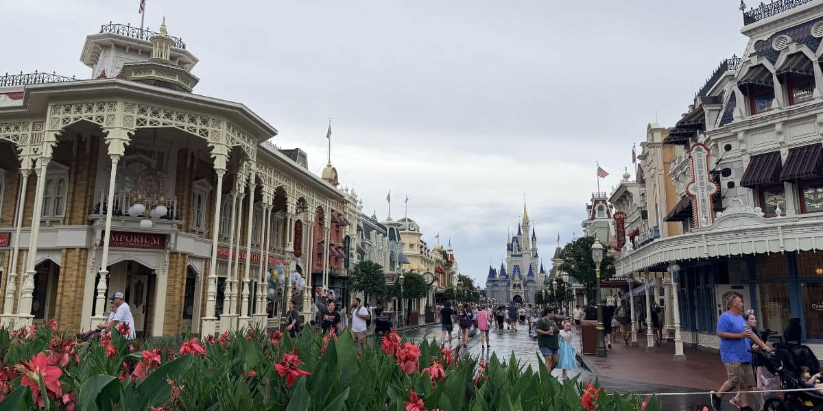 Main Street at Disney World bustles with excitement as a guest strolls past colorful flower beds, Cinderella Castle rising in the background beneath dramatic clouds—capturing the quintessential Disney charm that keeps fans returning, even amid news of occasional Disney World lawsuits.
