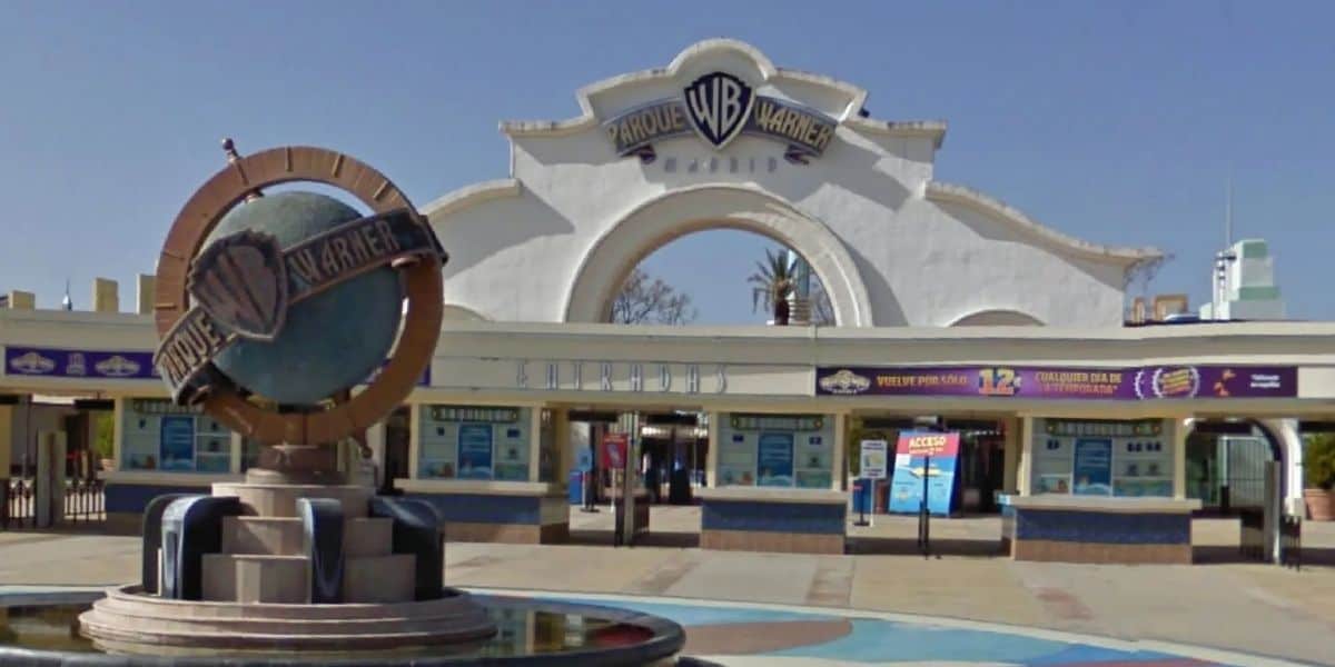 The grand entrance to Parque Warner Madrid featuring the iconic Warner Bros. shield statue, with ticket booths welcoming guests in the background.
