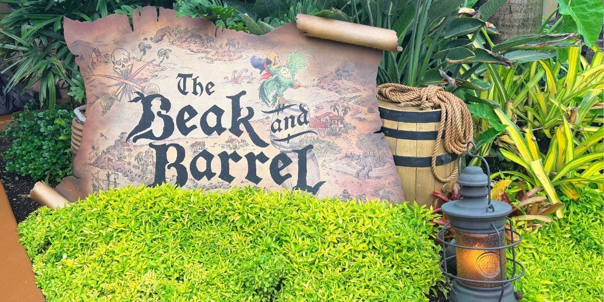 The Beak and Barrel sign welcomes guests with lush greenery, rustic barrels, and a lantern, perfectly capturing the whimsical Magic Kingdom vibe at Disney World.