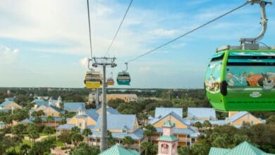 Brightly colored Disney Skyliner gondolas glide above the Caribbean Beach Resort, whisking guests over sparkling blue rooftops and swaying palm trees under a sunny Florida sky, promising park fans an unbeatable aerial view of the magic below.