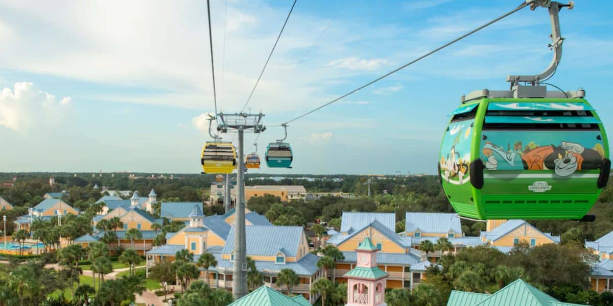 Brightly colored Disney Skyliner gondolas glide above the Caribbean Beach Resort, whisking guests over sparkling blue rooftops and swaying palm trees under a sunny Florida sky, promising park fans an unbeatable aerial view of the magic below.