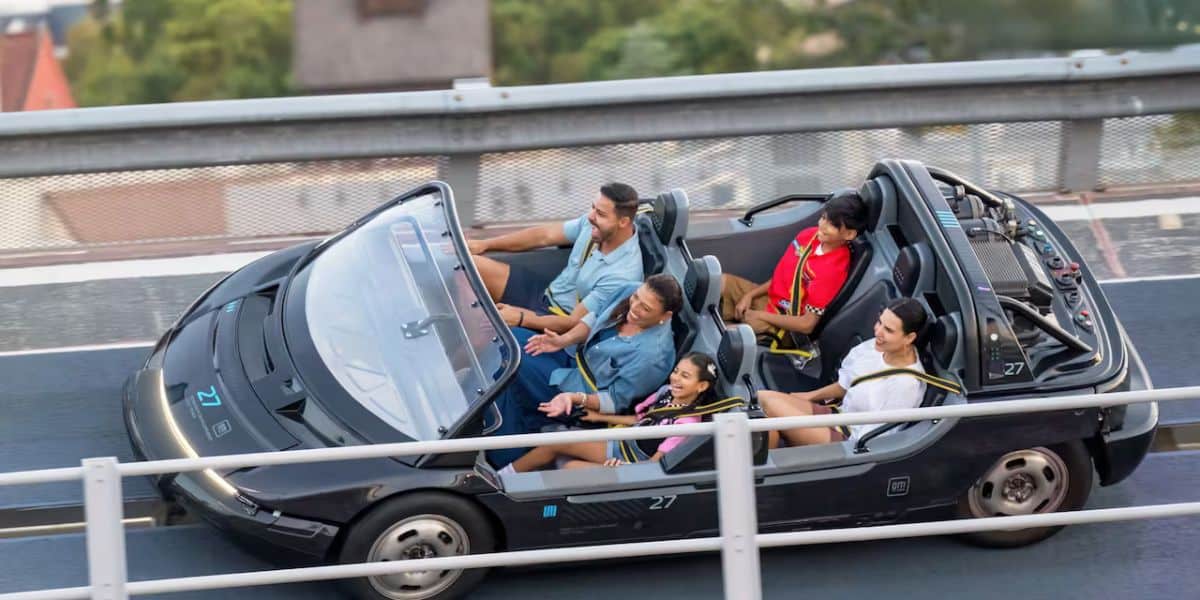 Guests enjoy the thrill of Test Track at EPCOT, smiling and laughing together in a sleek black ride vehicle as it zips along the track—caught up in the excitement, unaware that this fan-favorite attraction has been unexpectedly closed for over 24 hours with no word from Disney World.