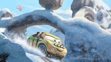 A cheerful, animated ride vehicle with happy guests inside winds through snow-capped mountain scenery, while a bright red helicopter attraction soars overhead.