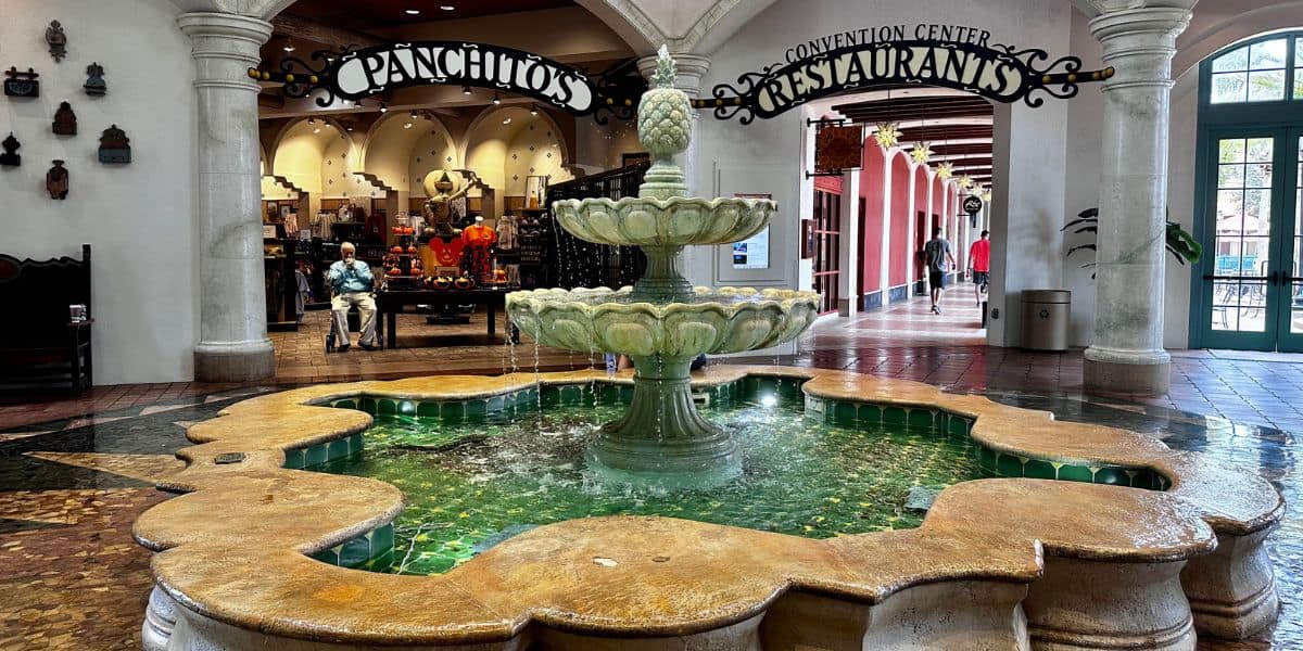 Charming stone fountain at Disney World’s indoor plaza, with nearby seating for guests to relax and enjoy views of gift shop displays and popular restaurant signs.