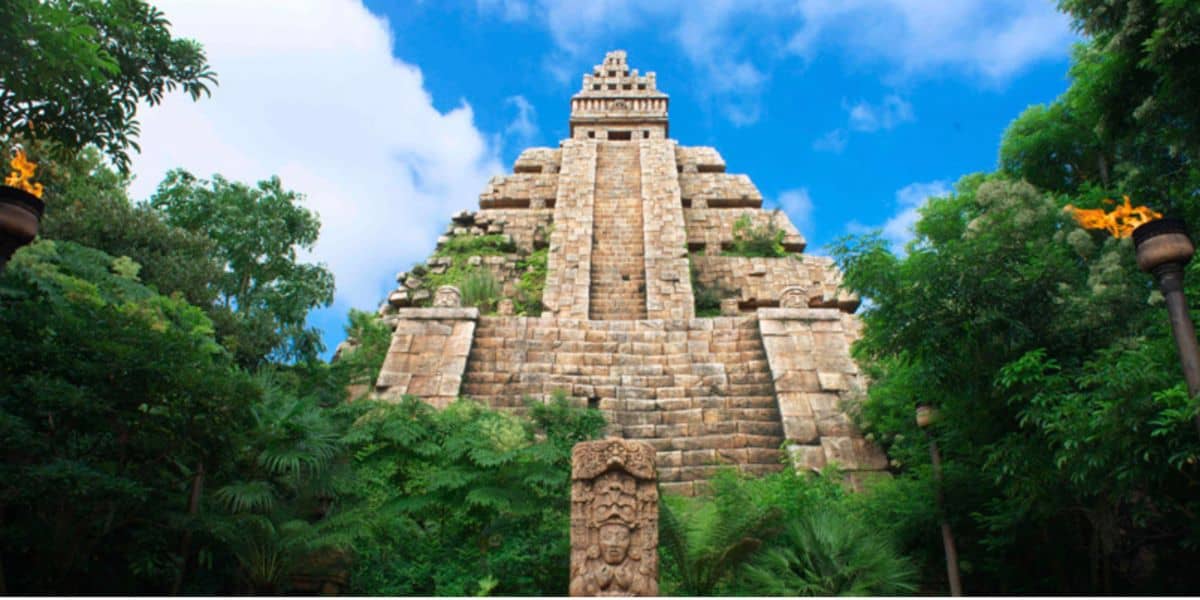 The iconic Indiana Jones Adventure temple at Disneyland, featuring its steep staircase and dramatic stone facade, nestled among vibrant jungle greenery beneath a bright blue sky.