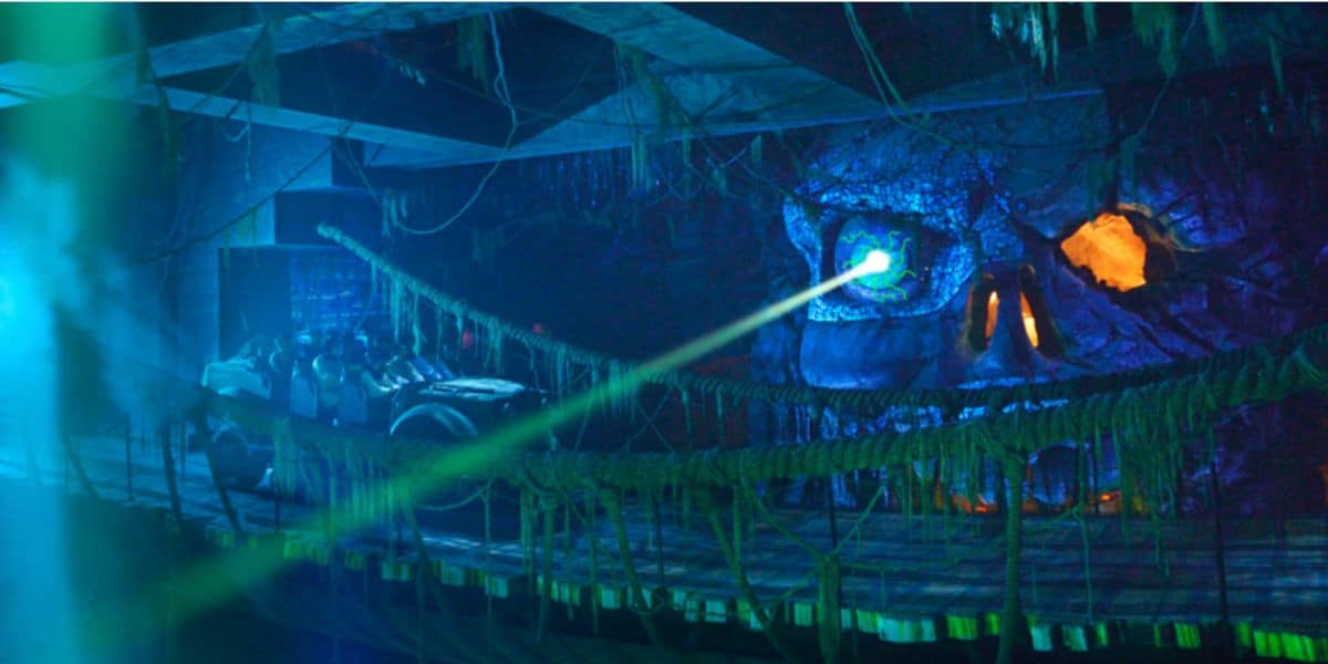 An Indiana Jones Adventure ride vehicle races past a glowing skull cave radiating eerie green light, while dynamic blue and orange lighting amps up the excitement—showcasing new thrills as this iconic Disneyland attraction returns with electrifying updates.