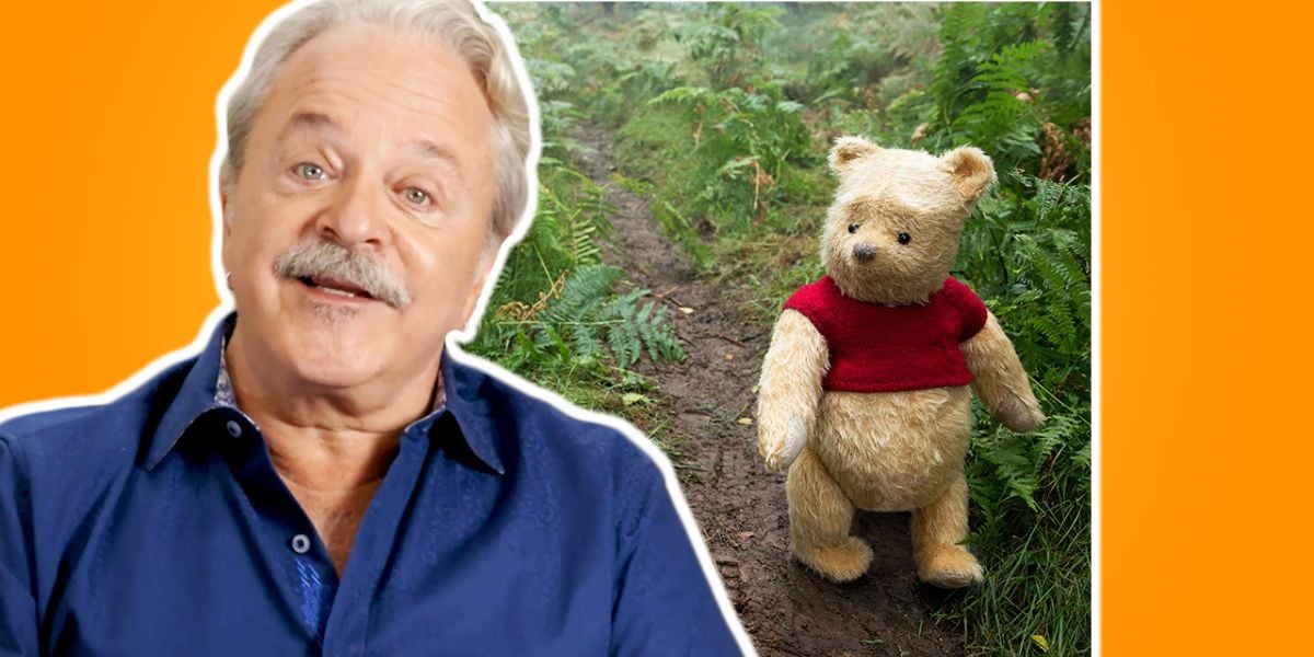 A smiling guest in a blue shirt poses with Winnie the Pooh on an enchanting forest path, set against a cheerful orange backdrop, celebrating Disney Legends and the unforgettable voice behind Pooh at a magical Disney experience.