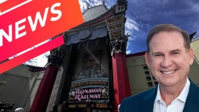 Walt Disney World President Joe Schott beams with excitement at the entrance to Runaway Railway, ready to greet guests as cheerful “NEWS” banners and a bright blue sky set the scene for a magical day.