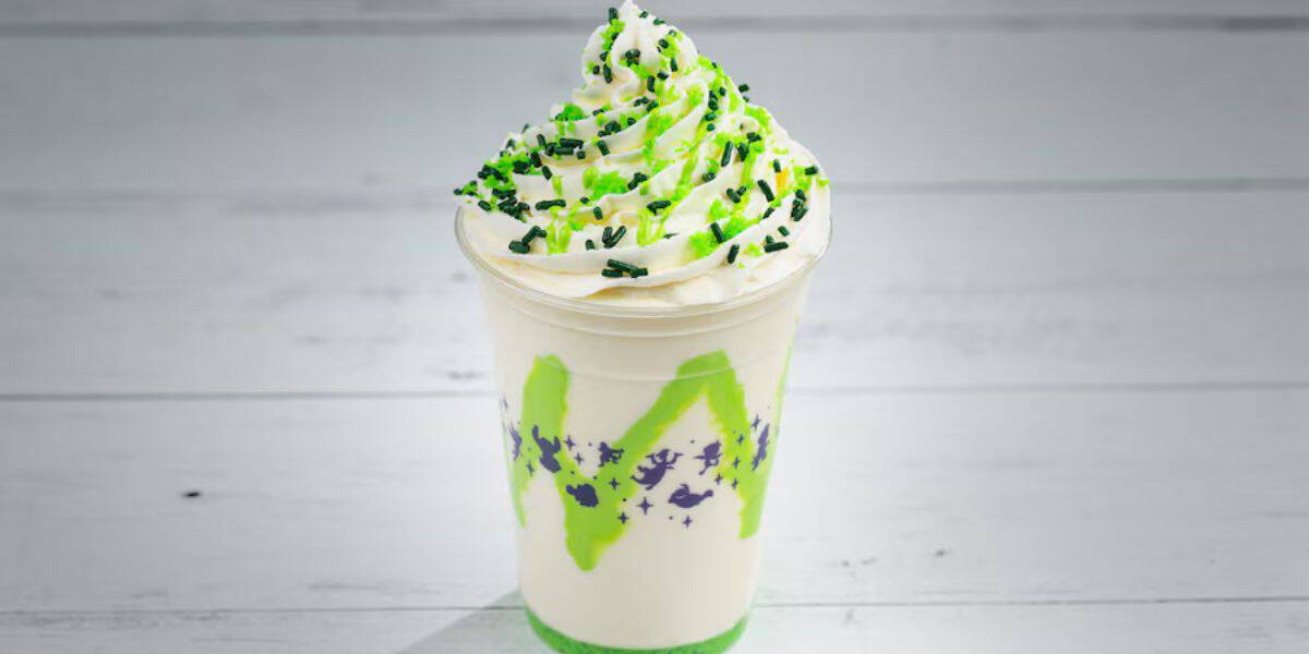 A festive vanilla milkshake at Universal Studios, topped with green syrup, a swirl of whipped cream, and green and black sprinkles, served in a clear souvenir cup.