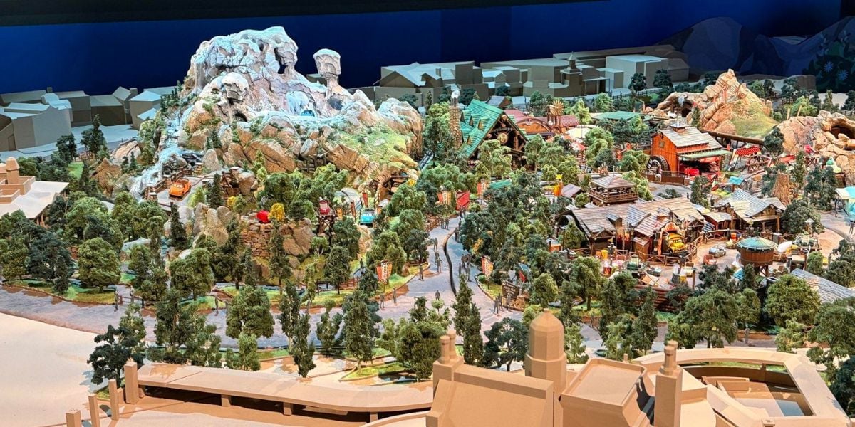 A scale model of a theme park featuring iconic attractions, lush landscaping with mountains and trees, signature buildings, and meandering pathways inviting guests to explore every area of the park.