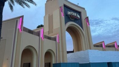 The iconic Universal Studios Florida entrance arch glows with vibrant pink lighting at dusk, welcoming guests even as construction barriers line the front plaza.