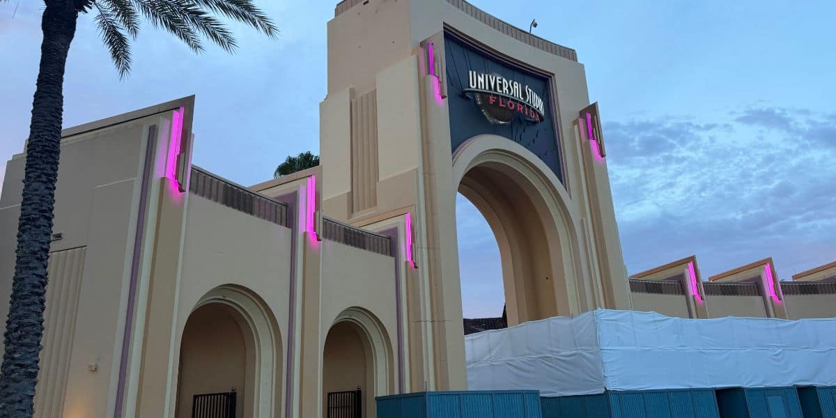 The iconic Universal Studios Florida entrance arch glows with vibrant pink lighting at dusk, welcoming guests even as construction barriers line the front plaza.