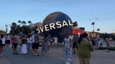 Guests gather around the iconic Universal globe statue at Universal Studios, surrounded by swaying palm trees.
