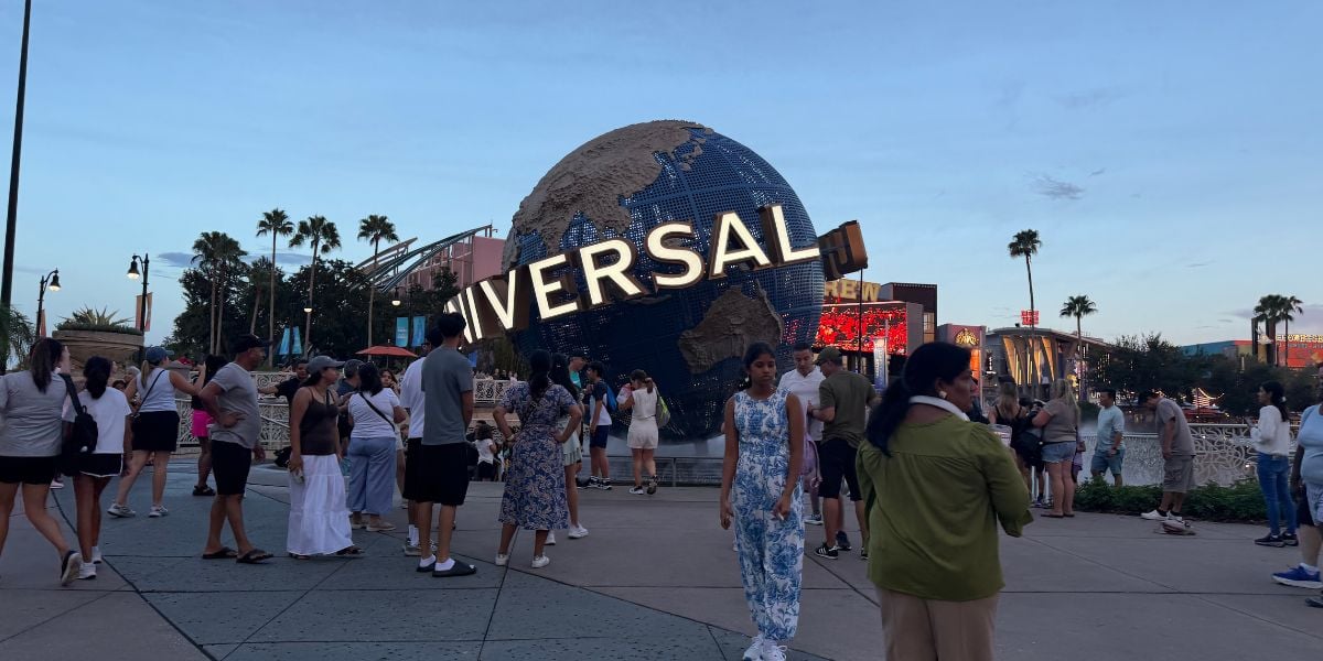 Guests gather around the iconic Universal globe statue at Universal Studios, surrounded by swaying palm trees.