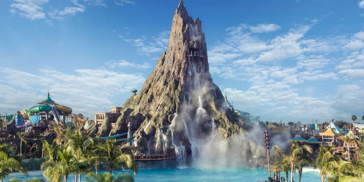 The towering Krakatau volcano water slide at Universal’s Volcano Bay is surrounded by swaying palm trees and set against a brilliant blue sky—making it the ultimate backdrop for thrilling rides, whether day or night during your Orlando visit.