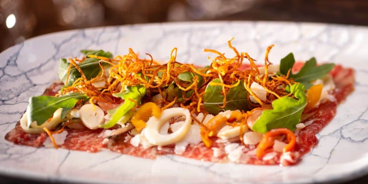 A mouthwatering plate of thinly sliced raw beef, dressed up with fresh greens, crispy fried onions, cheese, and colorful veggies takes center stage at Disney World’s steakhouse—a fan-favorite signature dish making its triumphant return after the grand reopening.