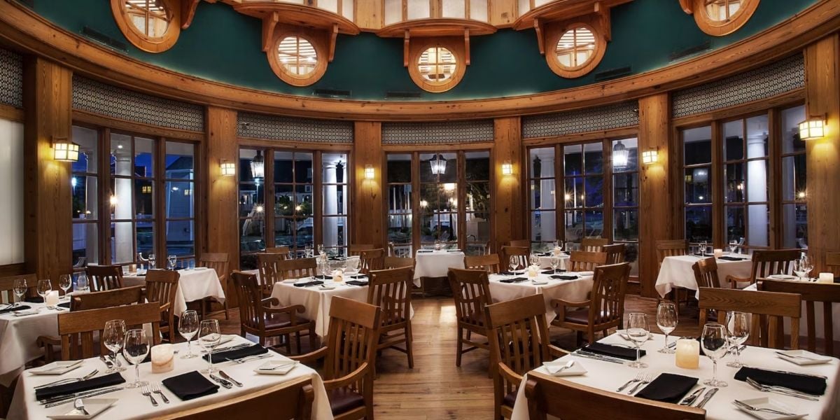 Round steakhouse restaurant with warm wooden accents and neatly set tables, where large windows frame the nighttime view—an upscale dining experience capturing the magical ambiance and premium feel you’d expect from a signature Disney World location.