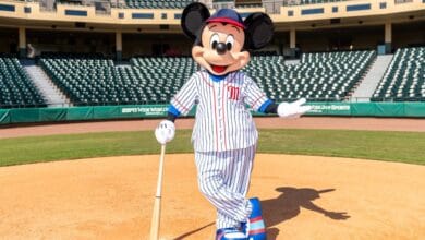 Mickey Mouse, decked out in his classic striped baseball uniform, grins on a lively baseball field at Disney World, gripping his bat and getting ready for the exciting Banana Bowl Championship—catch all the fun exclusively on Disney+ in 2026.
