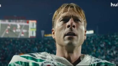 Chad Powers, suited up in his football uniform, gazes upward beneath the dazzling stadium lights, with the energetic crowd and scoreboard behind him capturing all the excitement and showtime spirit of game day.