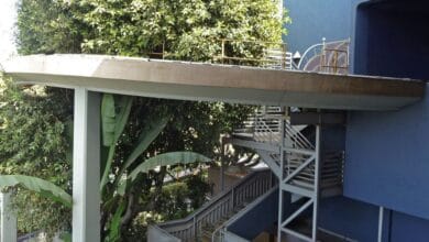 A winding concrete path dramatically ends in midair next to a staircase, creating an illusion of adventure beside lush greenery—like discovering a secret section of an imaginative theme park.